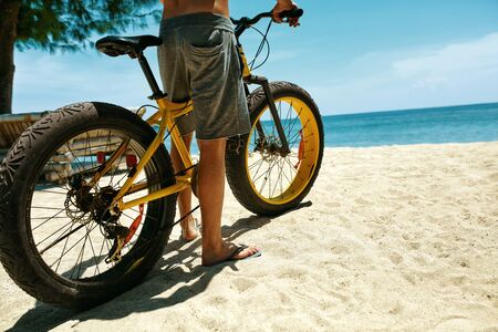 Summer Beach Sport. Close Up Of Man Legs Riding Yellow Sand Bicycle At Tropical Seaside. Fitness Male Model Exercising With Bike On Holiday Travel Vacation. Sporting Activity, Active Lifestyle Conceptの写真素材