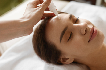 Face Skin Care. Closeup Of Beautiful Smiling Woman Receiving Serum Treatment In Beauty Salon. Cosmetologist Applying Cosmetic Serum On Girl's Face At Cosmetology Center. High Resolution Imageの写真素材