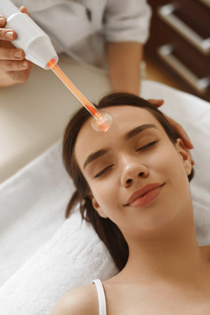 Face Beauty Treatment. Woman Getting Facial Darsonval Therapy Using High Frequency D'Arsonval, Skin Care Device For Anti Spot And Acne Treatment At Cosmetology Center. High Resolution Imageの写真素材