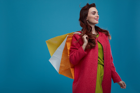 Woman Shopping. Fashion Model Walking With Colorful Shopping Bags. Happy Smiling Beautiful Sexy Girl In Stylish Fashionable Clothes With Paper Bag On Blue Background. Sales Concept. High Resolutionの写真素材