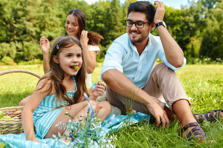 Family On Picnic. Happy Beautiful Young Family Spending Leisure Time Together In Park, Kids Eating Fruits And Having Fun In Nature. Smiling Parents And Children Relaxing Outdoors. Relationship Conceptの写真素材
