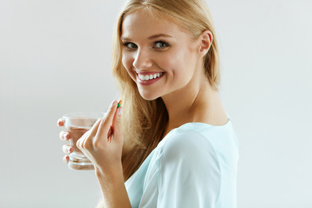 Healthy Diet Nutrition. Portrait Of Beautiful Smiling Young Woman Taking Vitamin Pill. Closeup Of Happy Girl Holding Colorful Capsule Pill And Glass Of Fresh Water. Dietary Supplement. High Resolutionの写真素材