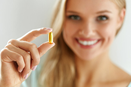 Vitamin And Supplement. Beautiful Smiling Woman Holding Fish Oil Capsule In Hand. Portrait Of Happy Girl Taking Pill With Cod Liver Oil, Omega-3. Diet Nutrition And Healthy Eating Lifestyle Concept.の写真素材
