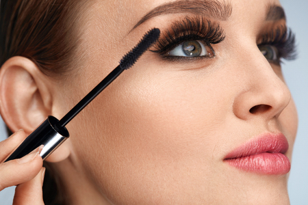 Facial Makeup. Beauty Woman Face With Fresh Healthy Skin And Perfect Professional Makeup. Young Woman With Long Fake Eyelashes Applying Black Mascara On Eyes With Brush. Cosmetics. High Resolutionの写真素材
