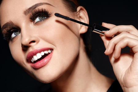 Beauty Makeup And Cosmetics. Closeup Of Beautiful Woman Face With Soft Skin, Perfect Professional Facial Make-up Applying  
Black Mascara On Long Thick Eyelashes With Cosmetic Brush. High Resolution