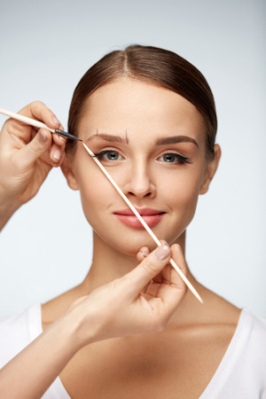 Woman Beauty. Portrait Of Beautiful Smiling Female Model With Perfect Skin, Face Makeup. Closeup Of Sexy Girl Modelling Eyebrows Shape With Stick And Brow Brush. Brows Correction. High Resolutionの写真素材