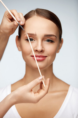 Eyebrows Correction. Beautiful Young Woman With Nude Face Makeup And Make-up Brow Brush. Closeup Portrait Smiling Sexy Female Model In Beauty Salon Forming Eyebrows Shape. Cosmetics. High Resolutionの写真素材