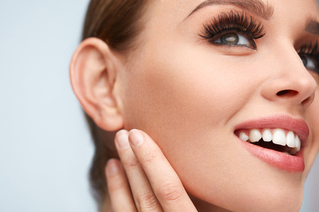 Long Black Eyelashes. Portrait Of Beautiful Sexy Young Woman With Smooth Soft Skin And Perfect Makeup. Smiling Female With Fake Eyelashes On Eyes Touching Her Face. Beauty Cosmetics. High Resolutionの写真素材