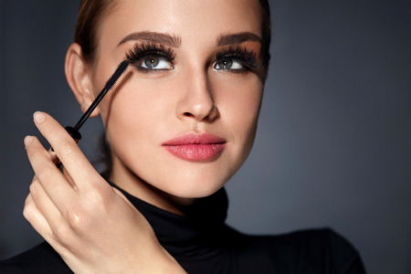 Mascara. Closeup Of Beautiful Young Woman Face With Beauty Makeup, Fresh Soft Skin And Long Black Thick Eyelashes Applying Mascara With Cosmetic Brush. Make-up And Cosmetics Concept. High Resolutionの写真素材