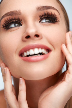 Beauty Woman Face. Closeup Of Glamorous Girl With Hands Touching Soft Smooth Skin. Portrait Of Beautiful Sexy Woman With Perfect Facial Makeup And Long Black Fake Eyelashes. Cosmetics. High Resolutionの写真素材