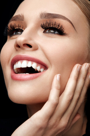 Long Black Eyelashes. Portrait Of Beautiful Sexy Young Woman With Smooth Soft Skin And Perfect Makeup. Smiling Female With Fake Eyelashes On Eyes Touching Her Face. Beauty Cosmetics. High Resolutionの写真素材