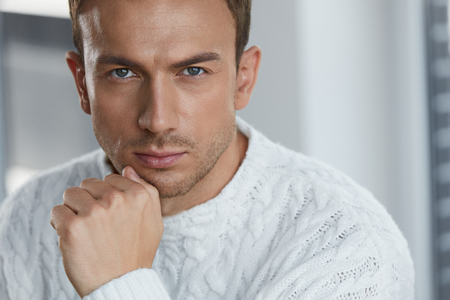 Handsome Young Man With Beautiful Face, Smooth Soft Facial Skin And Stubble Beard. Portrait Attractive Male Model In White Sweater Indoors. Beauty, Skin Care And Man's Health Concepts. High Resolutionの写真素材