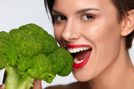 Healthy Diet. Beautiful Smiling Woman Eating Fresh Organic Broccoli. Closeup Of Female Face With Clean Skin, Red Lips Biting Green Vegetable. Healthy Foods, Vegetarian Nutrition And Health Conceptの写真素材