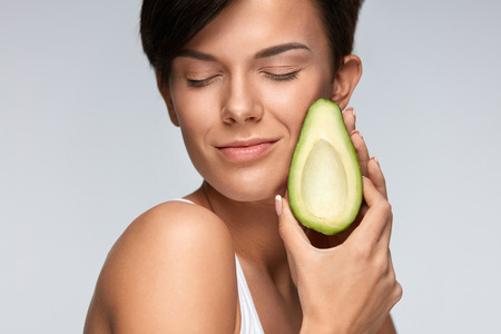 Skin Care And Beauty. Beautiful Happy Woman With Smooth Soft Clean Skin, Natural Makeup Holding Organic Green Avocado In Hand At Face. Healthy Lifestyle And Nutrition, Health Concept. High Resolutionの写真素材