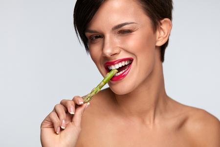 Woman On Diet Nutrition. Healthy Eating Girl With Beautiful Face, Pink Lips, White Teeth Biting Green Fresh Asparagus. Smiling Female Eating Vegetable. Good Food For Health And Beauty. High Resolutionの写真素材