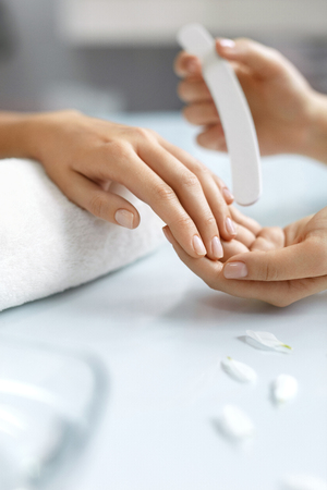 Spa Salon. Closeup Of Beautiful Woman Hands Having Nail Filing With Nail File By Manicurist. Close-up Of Beautician Hands Doing Cosmetic Procedure, Manicure On Female Hand. High Resolution Imageの写真素材