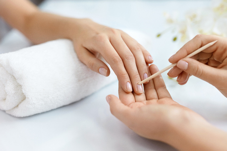 Nail Salon. Closeup Of Beautician Hands Cleaning Female Client's Nails With Orange Wooden Stick, Cuticle Pusher, Removing Cuticles In Beauty Salon. Woman Hands Nail Care And Manicure. High Resolutionの写真素材