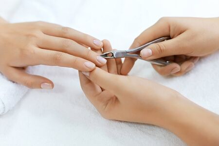Nails Beauty. Closeup Of Woman Hands Receiving Nail Care Treatment By Professional Manicure Specialist In Nail Salon. Manicurist Hands Cutting Cuticle On Nails With Nail Clippers. High Resolutionの写真素材