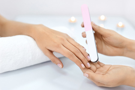 Nail Care. Closeup Of Female Hands Filing Nails With Professional Nail File In Beauty Nail Salon. Close-up Of Beautician Hands Doing Perfect Manicure On Woman's Hands. Nail Hygiene. High Resolutionの写真素材