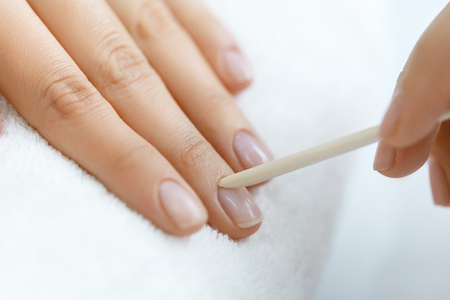 Beauty Care. Closeup Beautiful Woman Hand With Healthy Natural Nails Receiving Cuticle Removing Procedure With Wooden Cuticle Pusher Remover Stick In Salon. Manicure On Female Hands. High Resolutionの写真素材