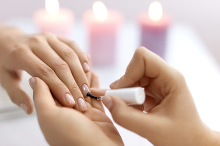 Nail Care And Manicure. Closeup Of Beautiful Female Hands Applying Transparent Nail Polish On Healthy Natural Woman's Nails In Beauty Salon. Manicurist Hand Painting Client's Nails. High Resolutionの写真素材