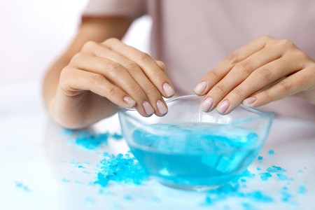 Spa Manicure. Woman Hands With Perfect Natural Healthy Nails Soaking In Aroma Hand Bath. Closeup Of Glass Bowl With Water And Blue Sea Salt For Spa Procedure. Professional Nail Care. High Resolutionの写真素材
