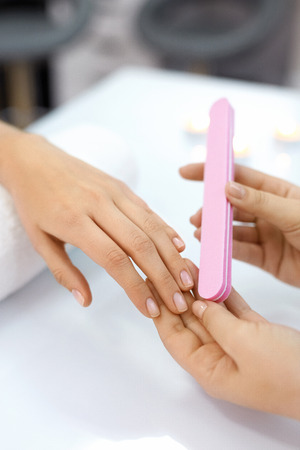 Female Manicure. Closeup Of Beautician Hands Polishing Woman Client's Nails With White Nail File In Beauty Spa Salon. Female Hand On Towel Polishing Nails. Nail Care And Hygiene. High Resolutionの写真素材