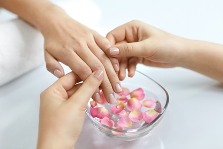 Nail Care. Woman Receiving Manicure Procedure In Spa Salon. Closeup Of Female Hands Getting Hand Massage From Beautician Near Aroma Bath For Hands With Flower Petals. High Resolutionの写真素材