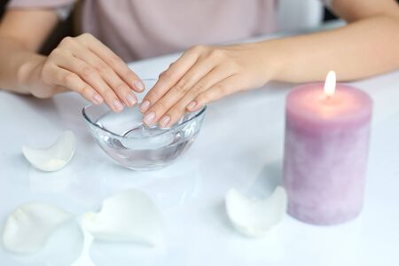 Spa Beauty Salon. Closeup Of Female Hands With Perfect Natural Fingernails Soaking In Hand Bath Before Manicure. Woman Washing Perfect Nails In Transparent Bowl Of Water. Nail Care. High Resolutionの写真素材