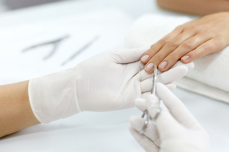 Nail Care. Closeup Of Beautician Hands Using Metal Cosmetic Nail Scissors For Cutting Cuticle From Female Client's Nails. Woman Hand Receiving Manicure Procedure With Nail Care Tool. High Resolutionの写真素材