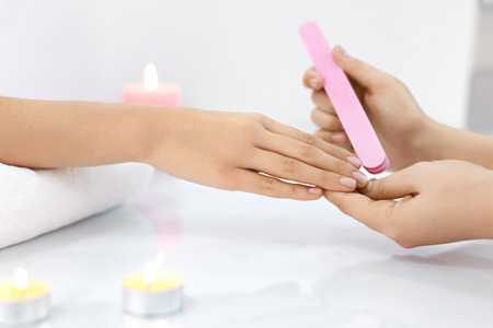Female Manicure. Closeup Of Beautician Hands Polishing Woman Client's Nails With White Nail File In Beauty Spa Salon. Female Hand On Towel Polishing Nails. Nail Care And Hygiene. High Resolutionの写真素材