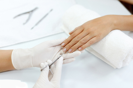 Manicure. Closeup Of Manicurist Hands Removing Cuticle From Female Nails With Professional Metal Nail Scissors. Woman Hand With Healthy Natural Nails Getting Nails Care Procedure. High Resolutionの写真素材