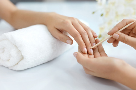 Nail Salon. Closeup Of Beautician Hands Cleaning Female Client's Nails With Orange Wooden Stick, Cuticle Pusher, Removing Cuticles In Beauty Salon. Woman Hands Nail Care And Manicure. High Resolutionの写真素材