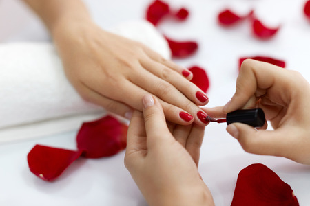 Manicure. Closeup Of Beautiful Woman Hands Polishing Nails With Red Nail Polish In Beauty Salon. Close-up Of Beautician Hand Painting Female Client Nails. Beauty Concept. High Resolutionの写真素材