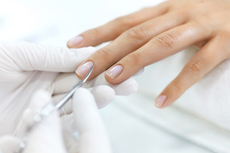 Manicure. Closeup Of Manicurist Hands Removing Cuticle From Female Nails With Professional Metal Nail Scissors. Woman Hand With Healthy Natural Nails Getting Nails Care Procedure. High Resolutionの写真素材