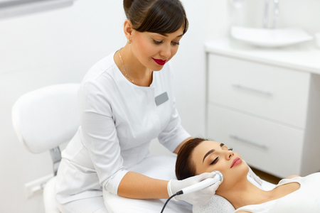 Beauty Treatment. Closeup Of Cosmetician Applying Cosmetics On Skin Of Beautiful Woman Using Ultrasound Phonophoresis Machine. Ultrasound Cavitation Procedure In Cosmetology Center. High Resolutionの写真素材