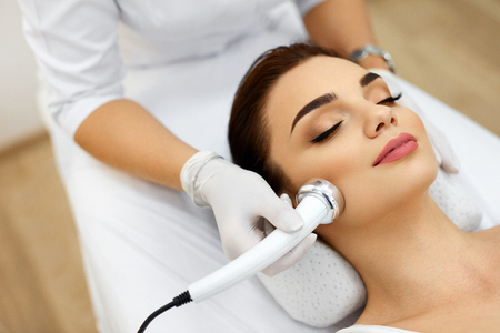 Cosmetology. Beautiful Woman Receiving Facial Skin Ultrasound Cavitation. Closeup Of Female Face Receiving Anti-Aging Cosmetics Using Ultrasound Cavitation Machine. Body Care. High Resolutionの写真素材