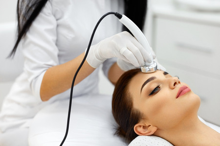 Cosmetology. Beautiful Woman Receiving Facial Skin Ultrasound Cavitation. Closeup Of Female Face Receiving Anti-Aging Cosmetics Using Ultrasound Cavitation Machine. Body Care. High Resolutionの写真素材
