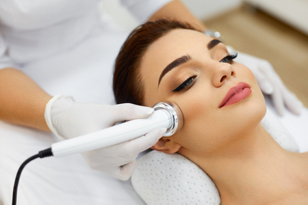 Cosmetology. Beautiful Woman Receiving Facial Skin Ultrasound Cavitation. Closeup Of Female Face Receiving Anti-Aging Cosmetics Using Ultrasound Cavitation Machine. Body Care. High Resolutionの写真素材