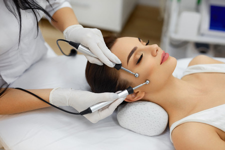Cosmetology. Beautiful Woman At Spa Clinic Receiving Stimulating Electric Facial Treatment From Therapist. Closeup Of Young Female Face During Microcurrent Therapy. Beauty Treatment. High Resolutionの写真素材
