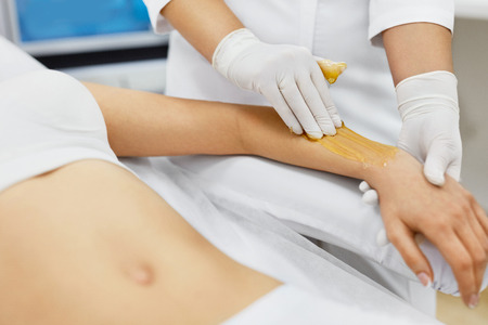 Hot Waxing. Beautiful Young Woman Getting Beauty Procedures For Hair Removal In Beauty Spa Salon. Closeup Of Beautician Applying Hot Wax On Female Client Hand. Skin And Body Care. High Resolutionの写真素材