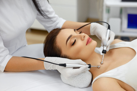 Cosmetology. Beautiful Woman At Spa Clinic Receiving Stimulating Electric Facial Treatment From Therapist. Closeup Of Young Female Face During Microcurrent Therapy. Beauty Treatment. High Resolutionの写真素材