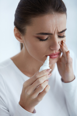 Cold. Portrait Of Beautiful Young Woman Sniffing Nasal Spray Closing One Nostril. Closeup Of Female Feeling Sick With Running Nose Using Sinus Medication For Blocked Nose. Healthcare. High Resolutionの写真素材