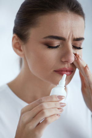Cold. Portrait Of Beautiful Young Woman Sniffing Nasal Spray Closing One Nostril. Closeup Of Female Feeling Sick With Running Nose Using Sinus Medication For Blocked Nose. Healthcare. High Resolutionの写真素材