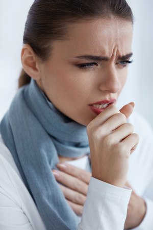 Woman Caught A Cold. Closeup Of Beautiful Sick Female In Scarf With Strong Cough Feeling Pain In Her Sore Throat. Portrait Of  Unhealthy Girl Coughing Indoors. Sickness And Illness. High Resolutionの写真素材