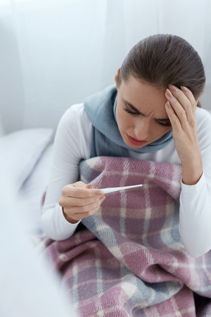 Fever And Cold. Portrait Of Beautiful Woman Caught Flu, Having Headache And High Temperature. Closeup Of Ill Girl Covered In Blanket, Feeling Sick Holding Thermometer. Health care. High Resolutionの写真素材