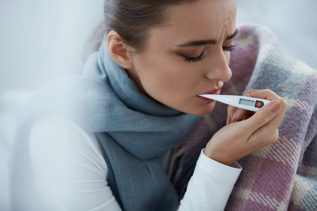 Woman Caught Cold. Closeup Of Beautiful Young Female Covered In Blanket Feeling Sick Holding With Thermometer In Mouth, Measuring Body Temperature. Portrait Of Ill Girl Having Fever. High Resolutionの写真素材