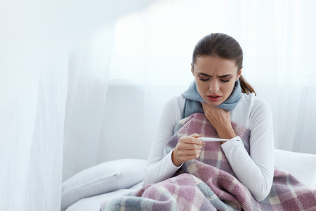Ill Woman Caught Cold, Having Fever And Measuring Temperature With Thermometer. Portrait Of Sick Girl With Sore Throat Covered In Blanket Having Health Problem. Illness Concept. High Resolutionの写真素材