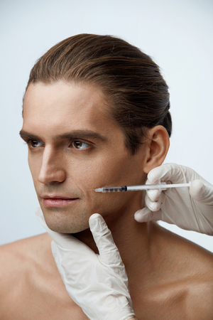 Face Procedure. Portrait Of Handsome Young Man Receiving Facial Lifting Injections. Closeup Of Beautician Hands Doing Cosmetic Injection On Male Cheekbone. Beauty Treatment Concept. High Resolutionの写真素材