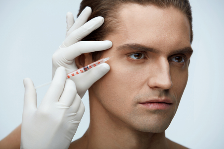 Facial Beauty. Portrait Of Handsome Man Getting Hyaluronic Collagen Injection. Closeup Of Beautician Hands Holding Syringe With Transparent Liquid Near Male Face. Skin Lifting. High Resolutionの写真素材